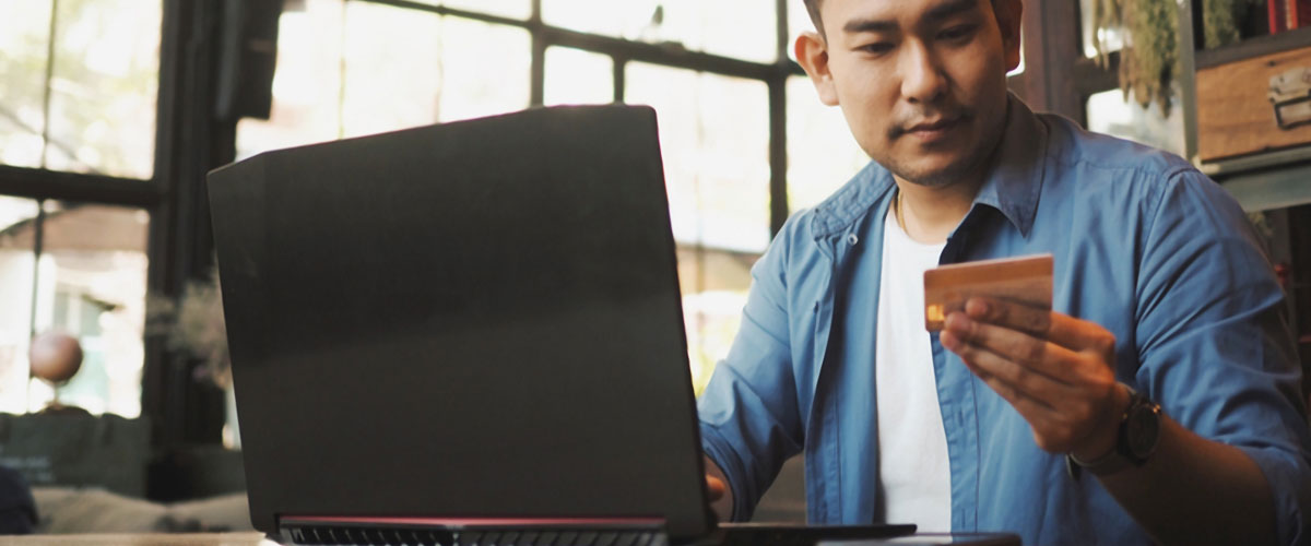 Smart young Asian man using credit card on laptop while drinking coffee at a desk