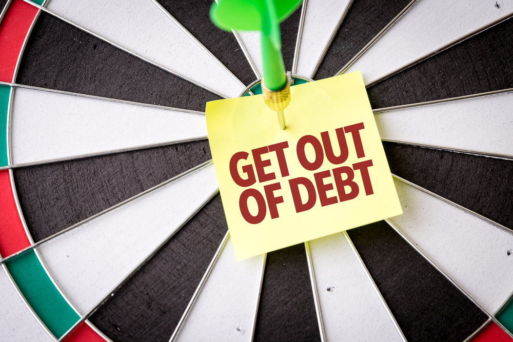 A dartboard with a green dart through a sticky note that says get out of debt.