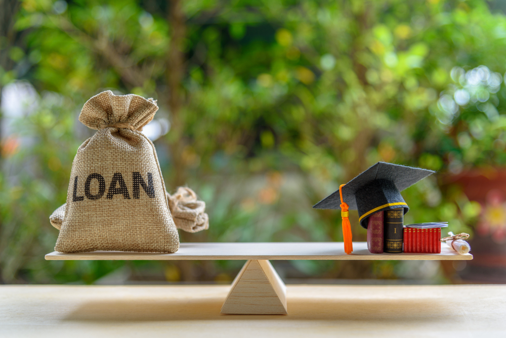 A balanced scale with a burlap loan bag on one end and a graduation cap, diploma and books on the other