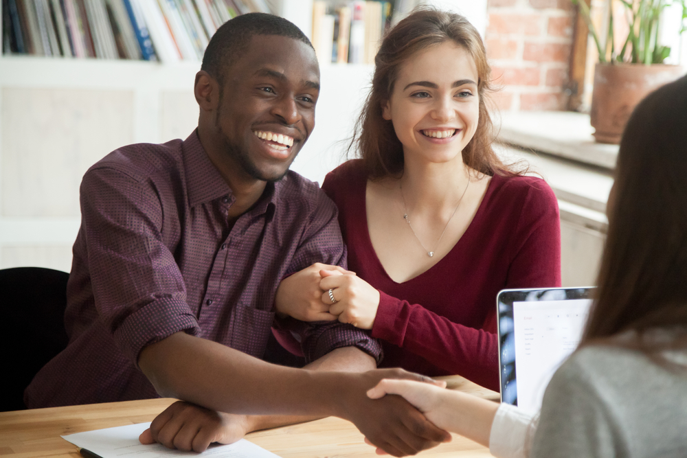 A young smiling multiracial couple shaking hands with a lender