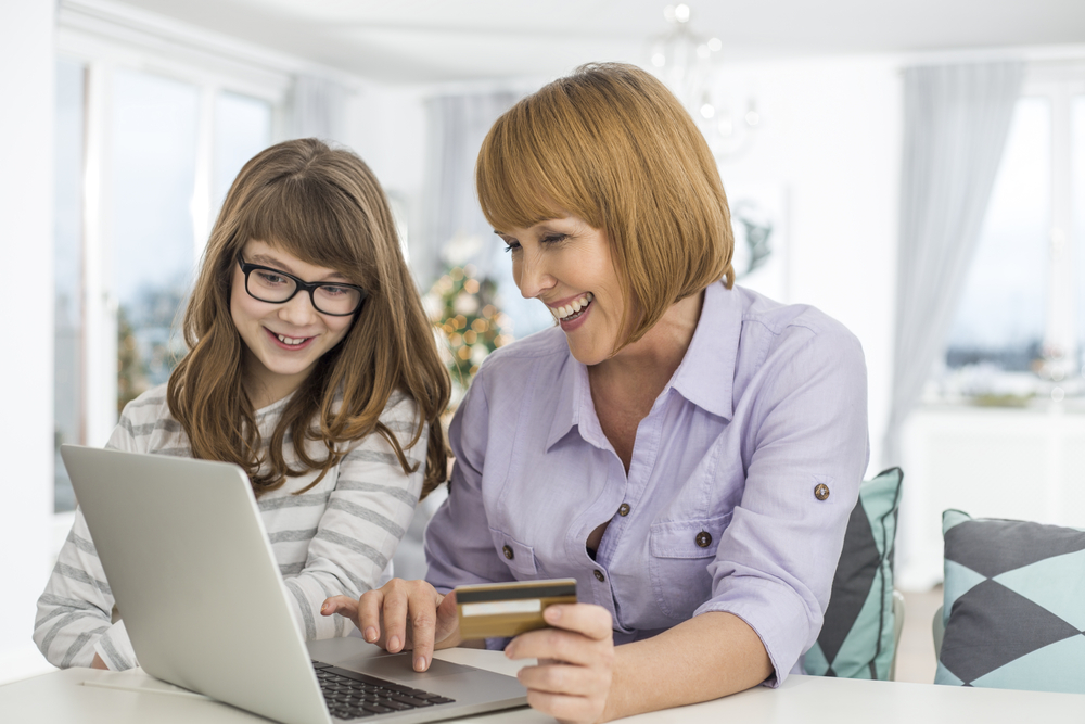 Cheerful mother with a credit card looking at laptop with teen daughter.
