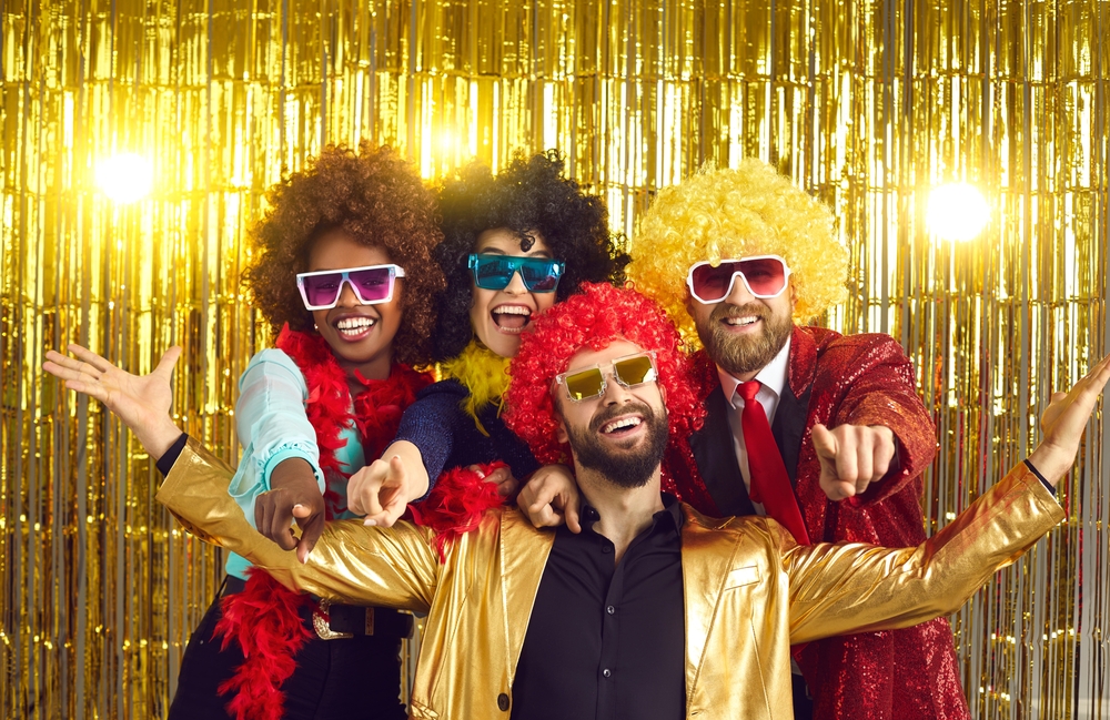 Four friends in 70s disco costumes pose for the camera.