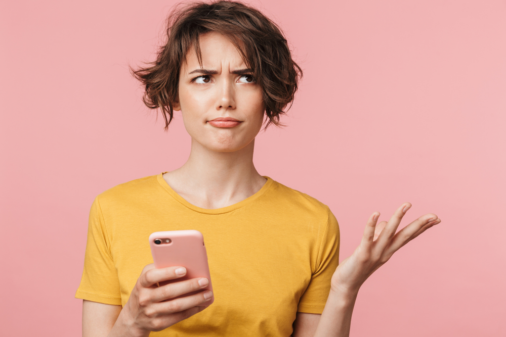 Confused young woman on mobile phone shrugs.