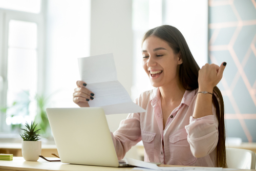 Happy young woman excited by reading good news in paper letter with open laptop