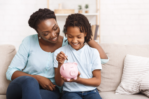 smiling mom and daughter putting money in a piggy bank