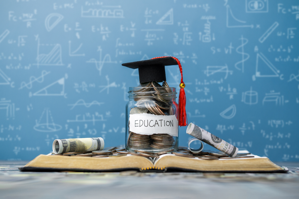 A jar of coins on a book with a graduation cap on top