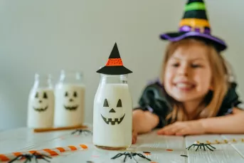 Little girl in witch costume reaching for Halloween decorations.