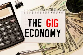 Notebook with text, "The GIg Economy," cash, and office tools