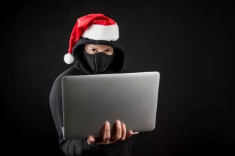 man in all black wearing a santa hat holding a laptop