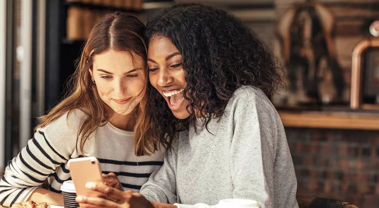 Two friends sharing a phone and excited about loan opportunities